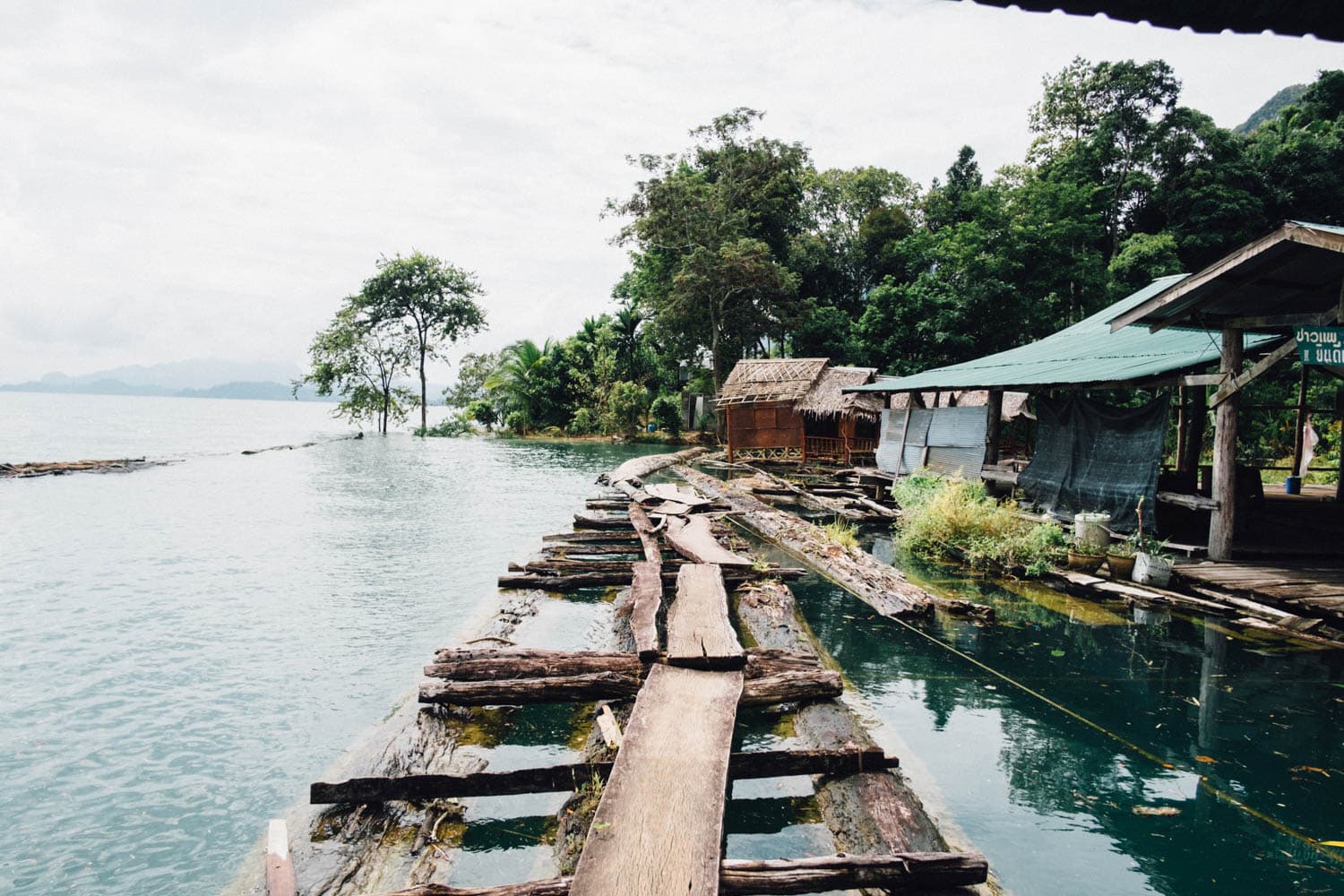 A wooden walkway connecting huts beside a lake
