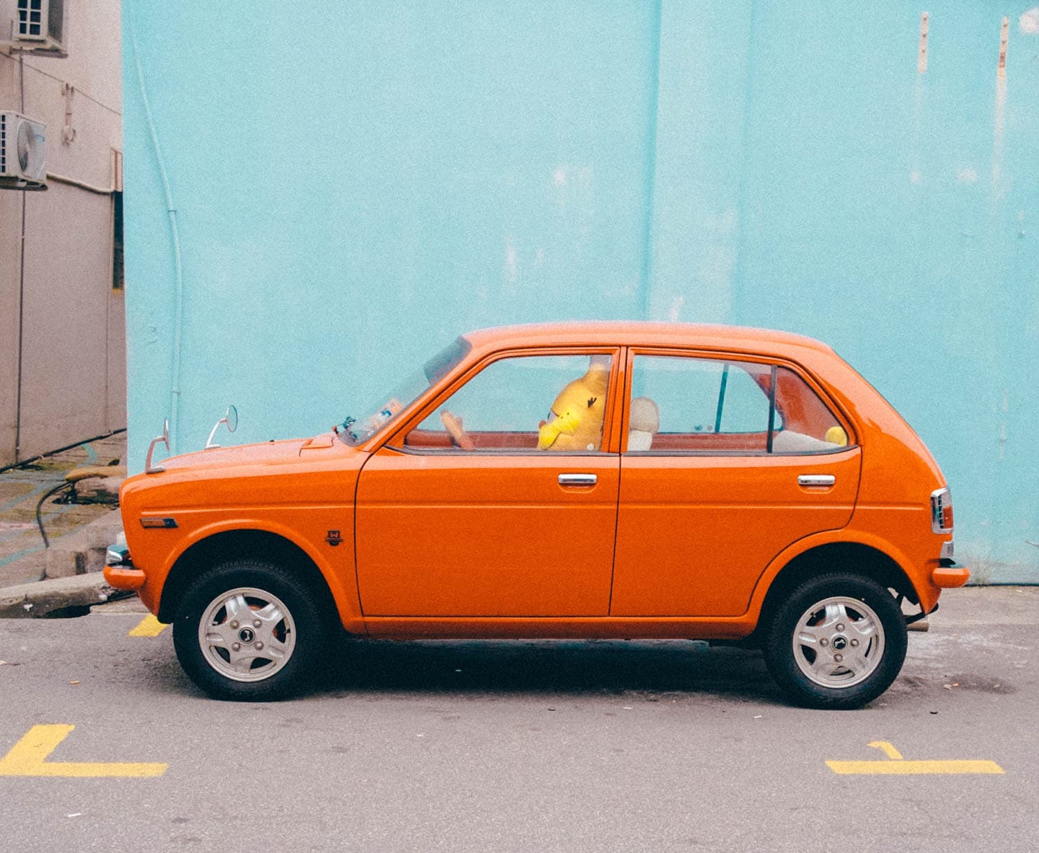 An orange compact car parked against a turquoise wall