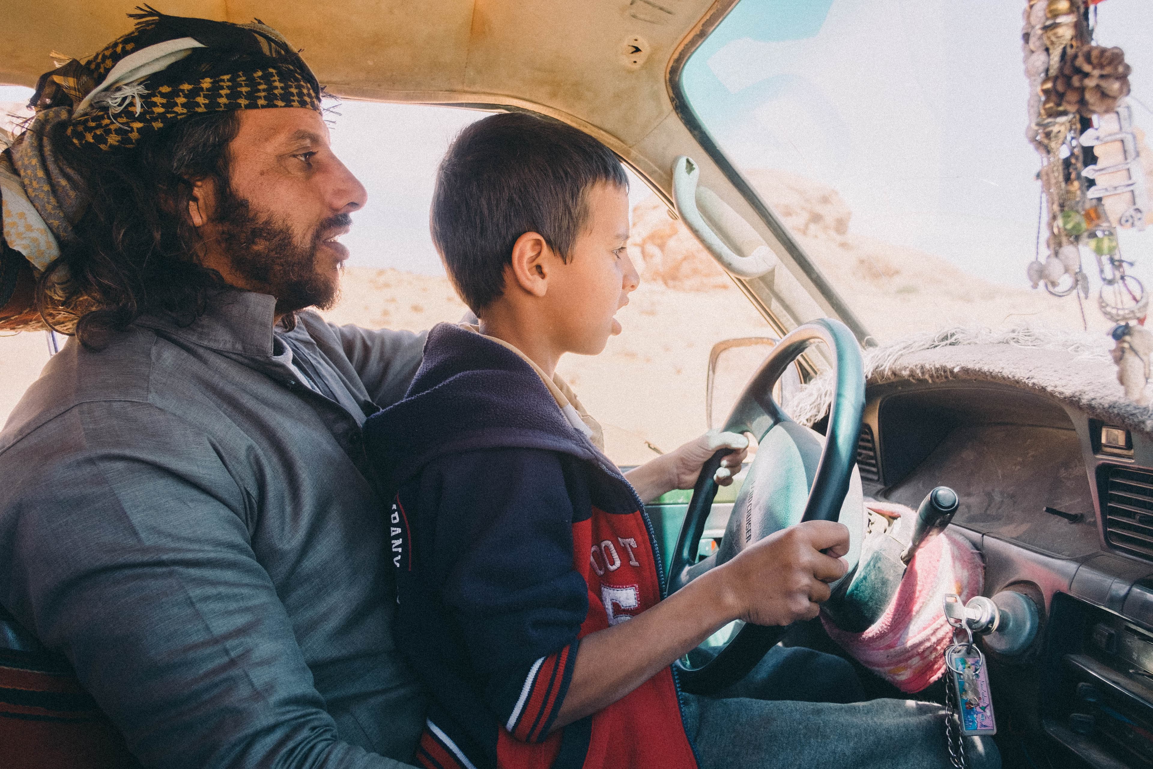 A man and a child travelling through the desert by car