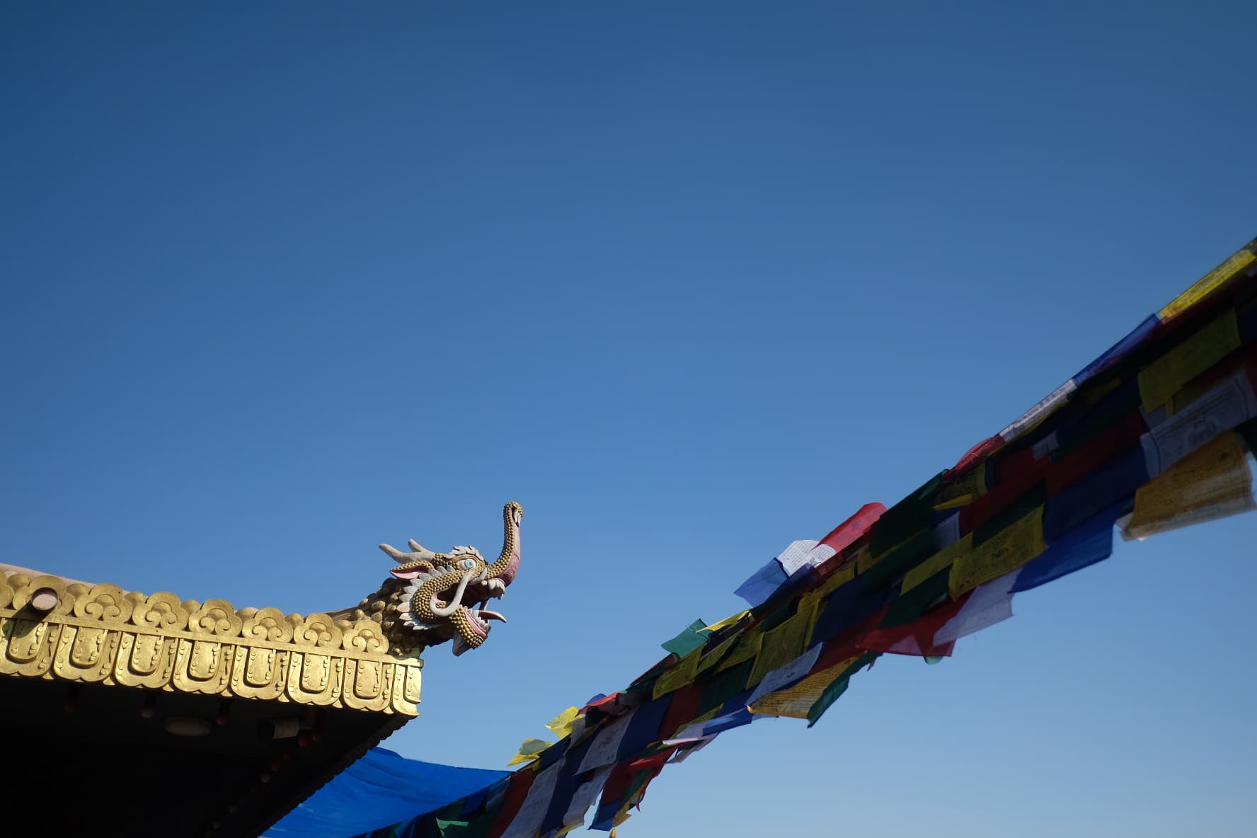 A carved temple roof and prayer flags against a blue sky