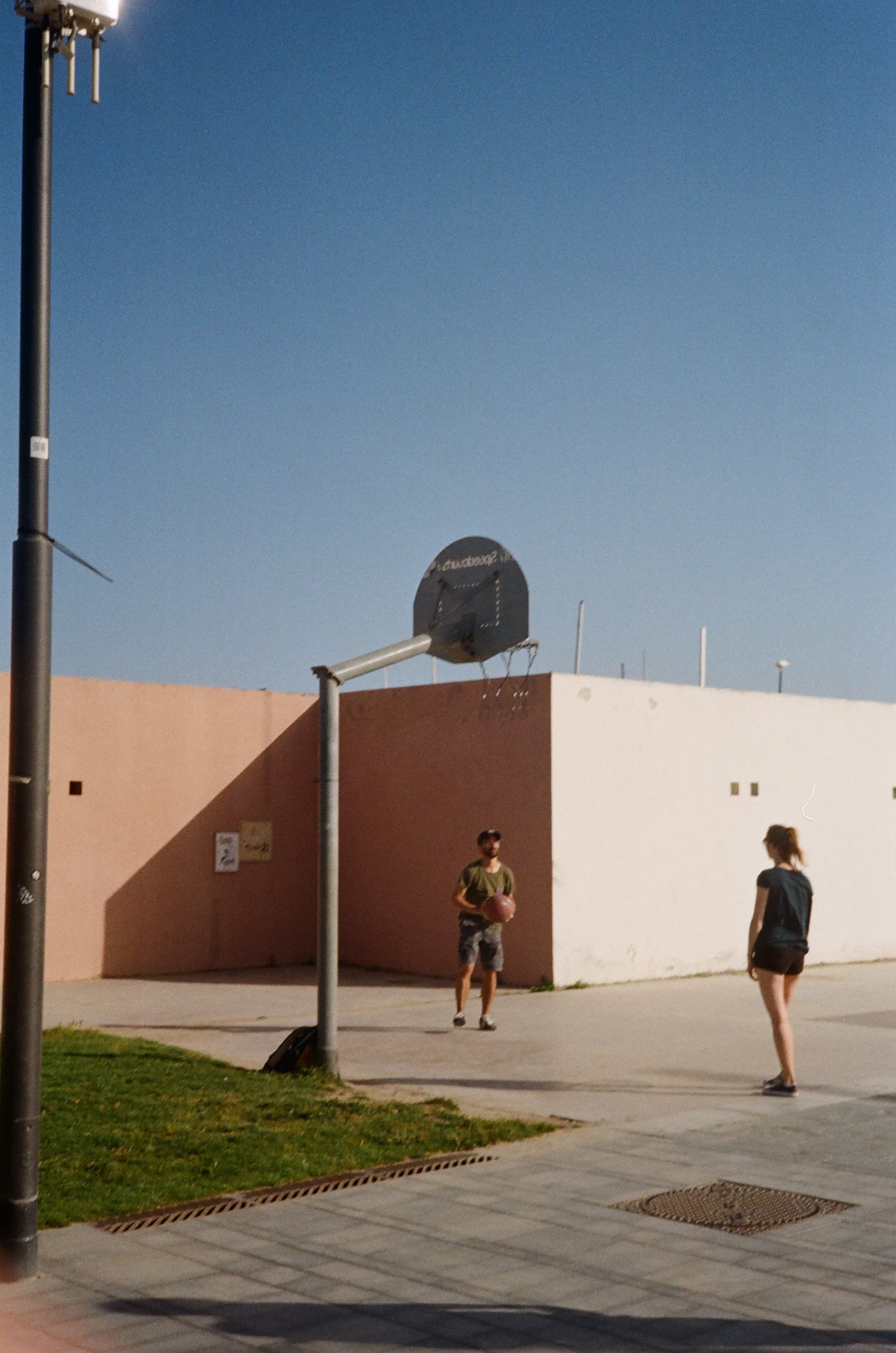 A person walking beside an outdoor basketball court