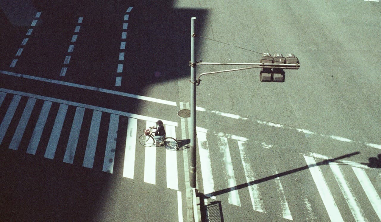 A cyclist crossing a sunlit intersection from above