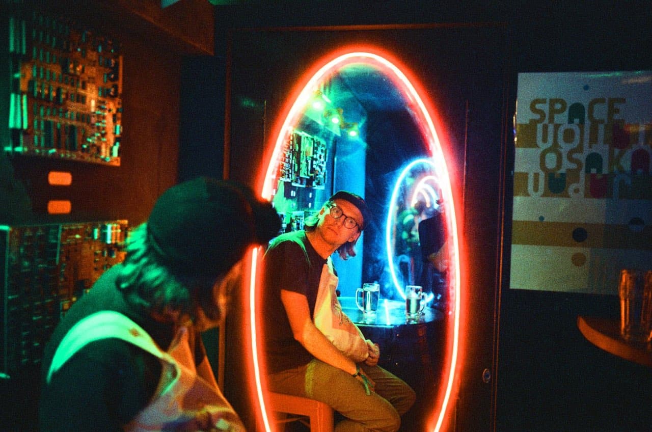People reflected in the neon mirror of a dimly lit bar