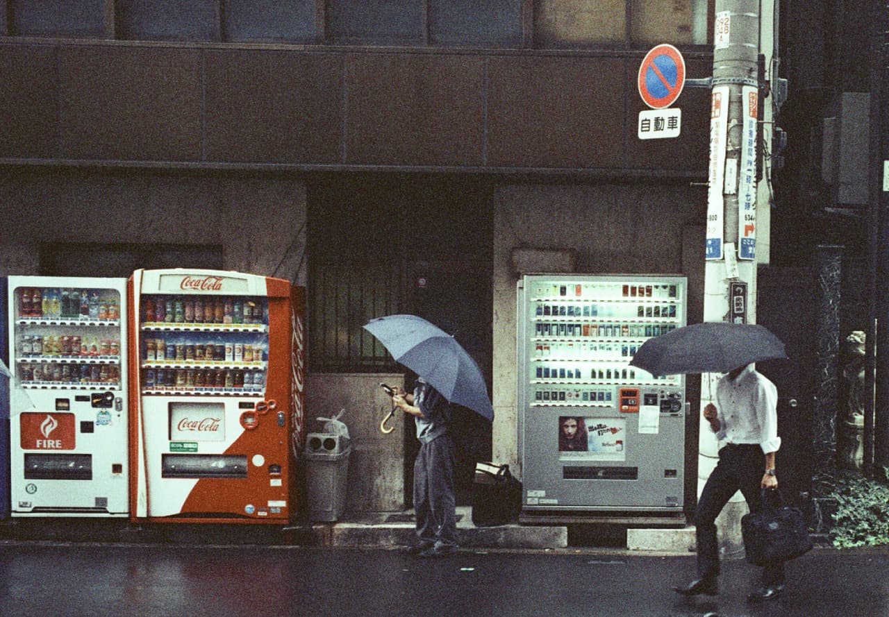 Pedestrians with umbrellas passing a row of vending machines