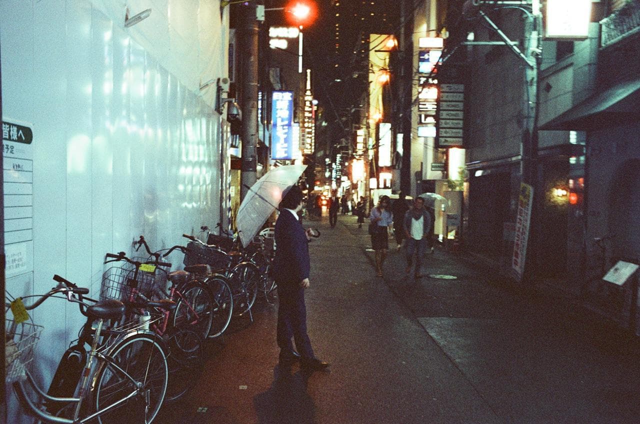 A person with an umbrella beside bicycles on a night street