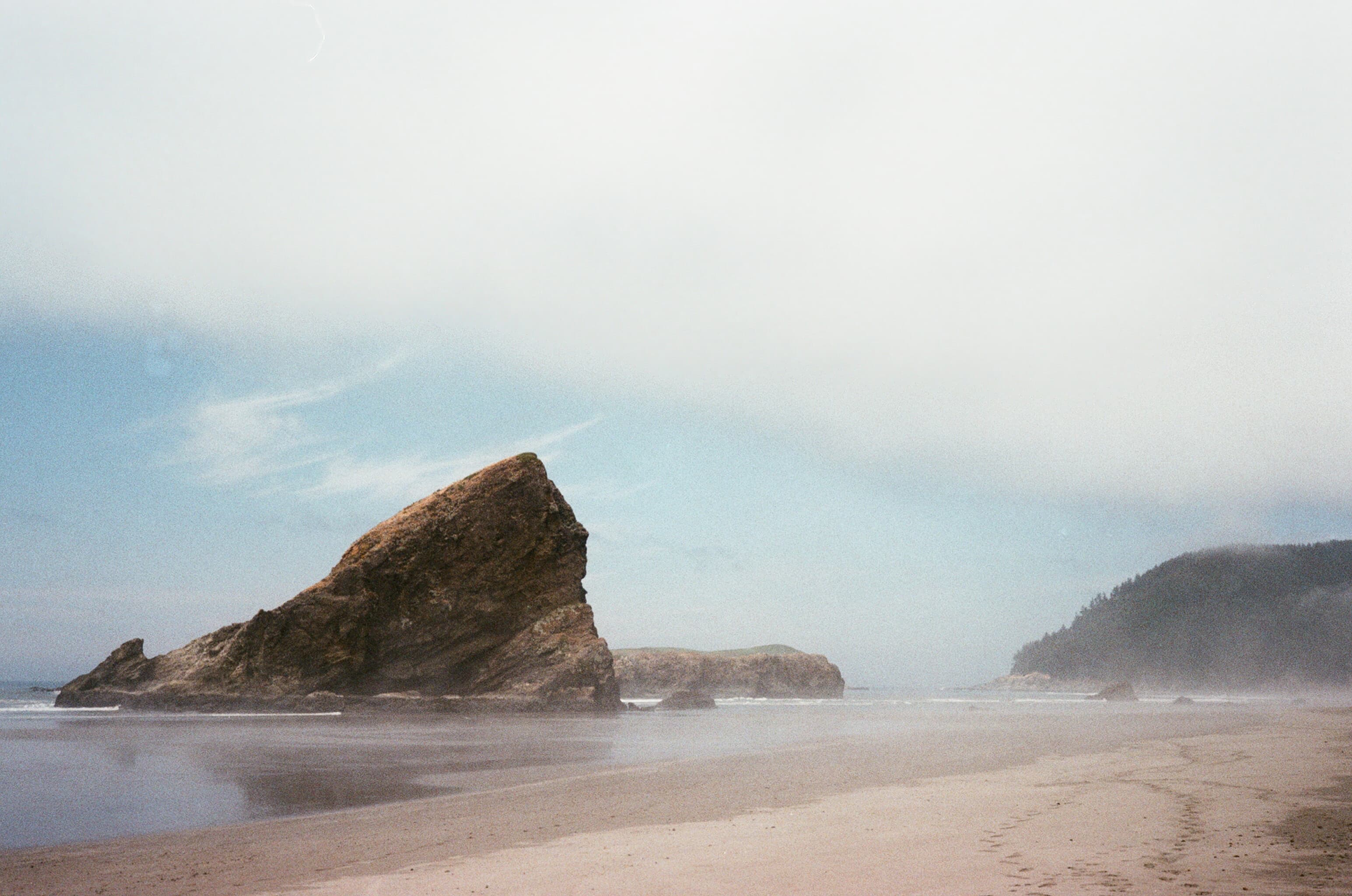 A sea stack rising from a misty beach