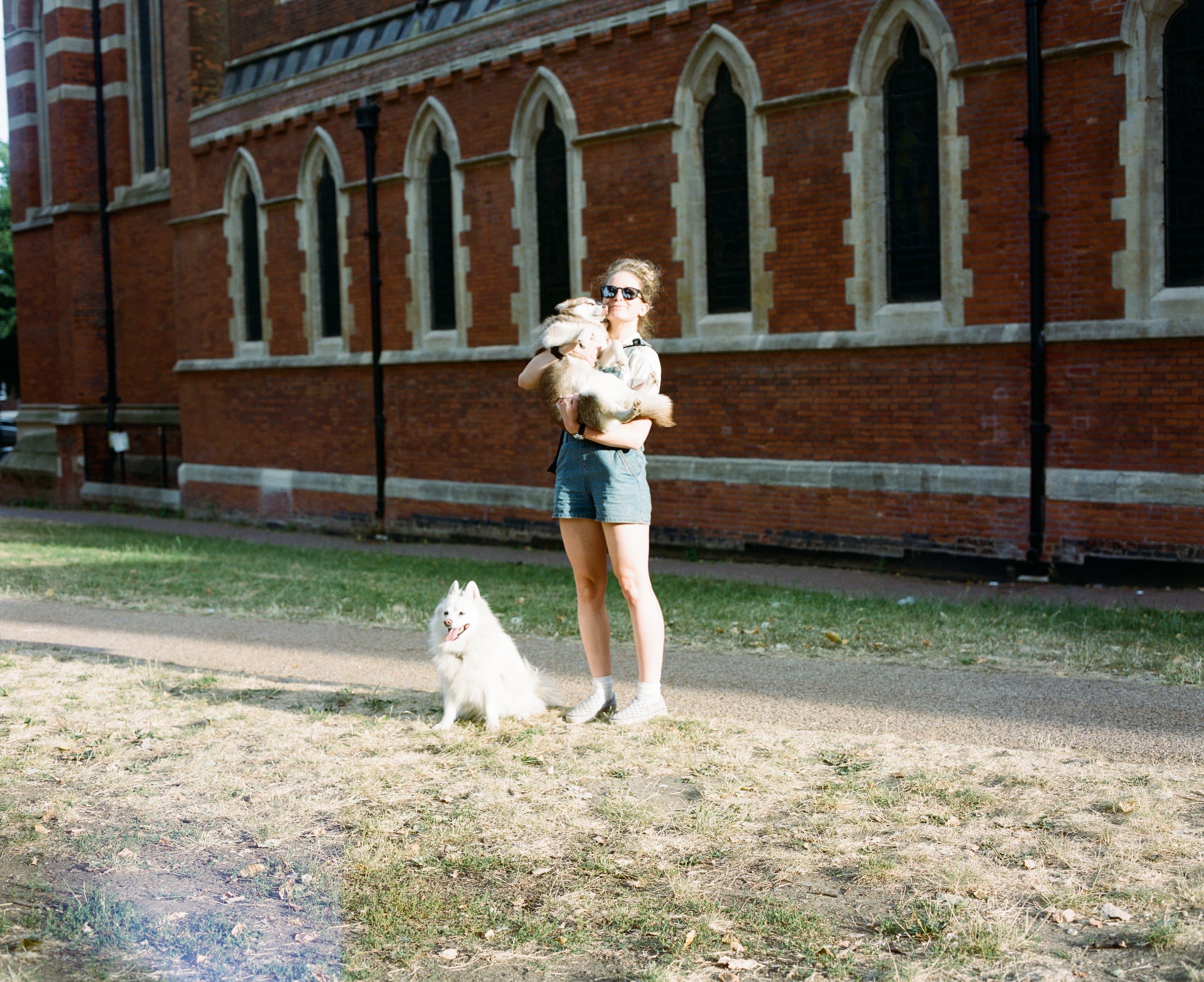 A person standing with two dogs beside a brick building