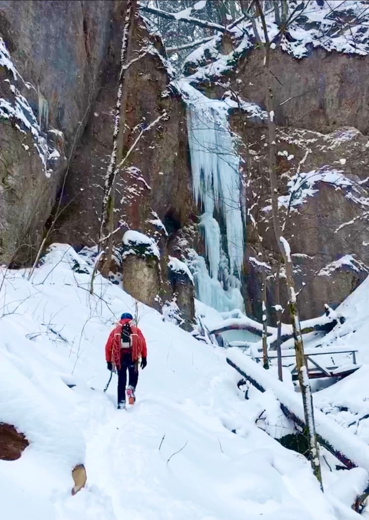 A hiker crossing a snow-covered rocky path